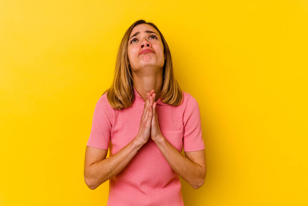 Sarı arka planda izole edilmiş genç, beyaz bir kadın el ele tutuşup ağza yakın dua ediyor, kendinden emin.. - Fotoğraf, Görsel