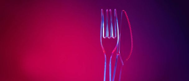 Plastic transparent fork and knife on red background - Valokuva, kuva