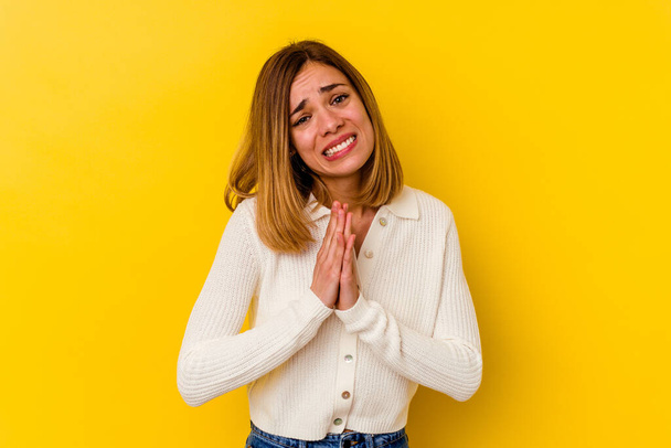 Giovane donna caucasica magra isolato su sfondo giallo tenendosi per mano in pregare vicino alla bocca, si sente fiducioso. - Foto, immagini