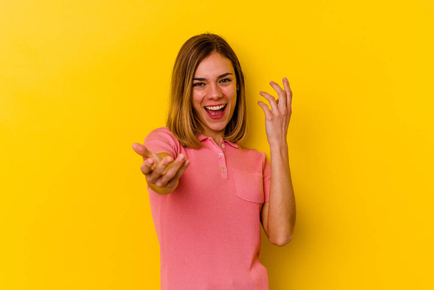Jeune femme maigre caucasienne isolée sur fond jaune pointant du doigt vers vous comme si vous invitant se rapprocher. - Photo, image