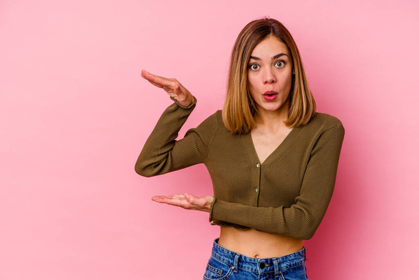 Young caucasian woman isolated on pink background shocked and amazed holding a copy space between hands. - Фото, зображення