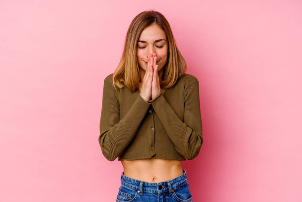 Giovane donna caucasica isolata su sfondo rosa tenendosi per mano in preghiera vicino alla bocca, si sente fiducioso. - Foto, immagini