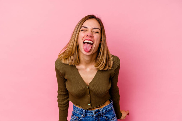 Joven mujer caucásica aislada sobre fondo rosa divertida y amigable sobresaliendo lengua. - Foto, imagen