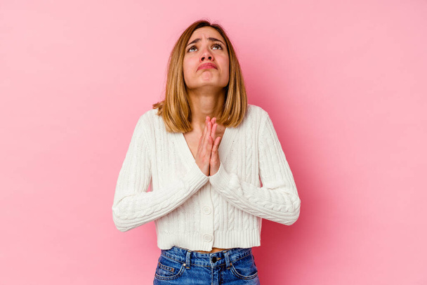 Jonge blanke vrouw geïsoleerd op roze achtergrond hand in hand bidden in de buurt van de mond, voelt vertrouwen. - Foto, afbeelding