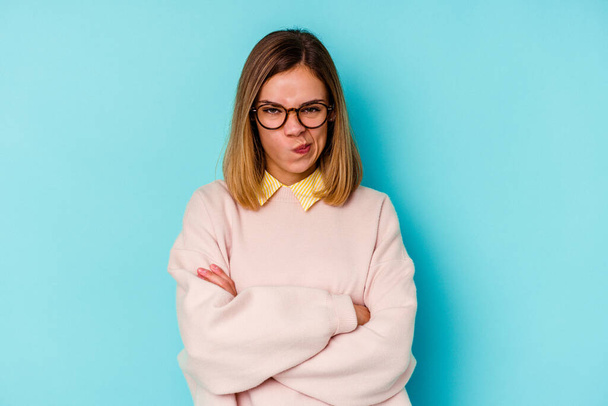 Young student caucasian woman isolated on blue background frowning face in displeasure, keeps arms folded. - Photo, Image
