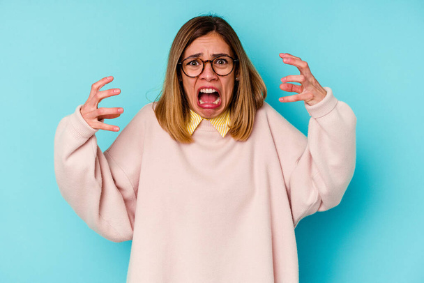 Young student caucasian woman isolated on blue background screaming with rage. - Photo, Image