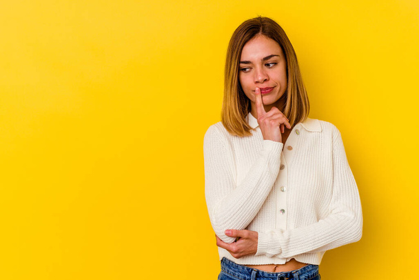 Young caucasian skinny woman isolated on yellow background looking sideways with doubtful and skeptical expression. - Photo, Image