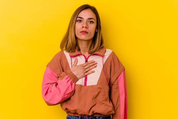 Young caucasian skinny woman isolated on yellow background taking an oath, putting hand on chest. - Foto, imagen