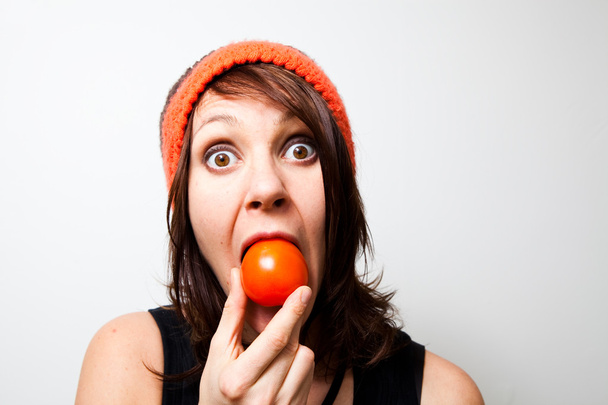 Jovem mulher a comer tomate. Expressão facial engraçada
. - Foto, Imagem