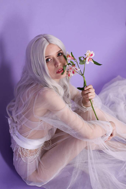 szőke sovány lány egy fehér átlátszó ruha egy lila háttér - Fotó, kép