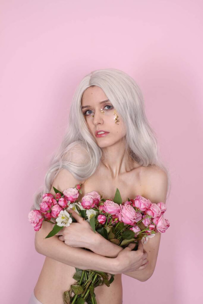 meztelen sovány lány kezében virágok rózsaszín háttér. barnahajú - Fotó, kép