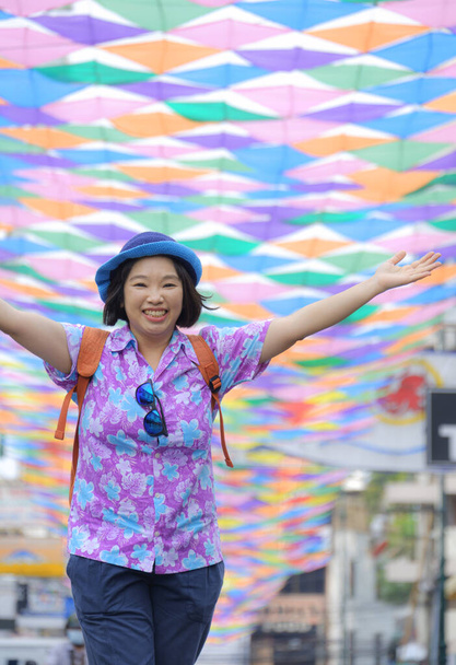 Mosolygó ázsiai női turista felemeli a kezét érzés vidám sétáló utcán színes dekoratív szövet lóg a levegőben függőleges keretben - Fotó, kép