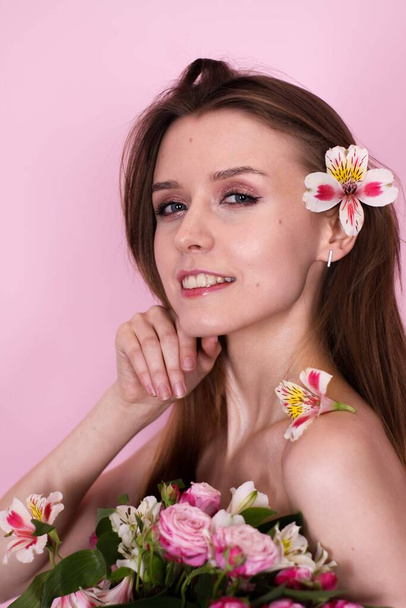 naked skinny girl holding flowers on a pink background. brunette - Zdjęcie, obraz