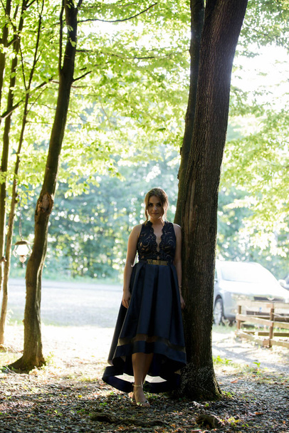 A vertical shot of a young woman standing in a tree shade in a blue dress - Foto, Bild