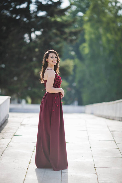 A closeup shot of a young woman posing in a red dress on a pathway and smiling - Φωτογραφία, εικόνα