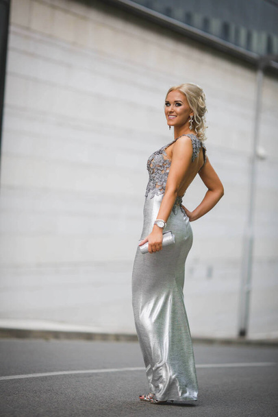 A shallow focus vertical shot of a young woman posing in a silver dress in front of a building - Foto, afbeelding