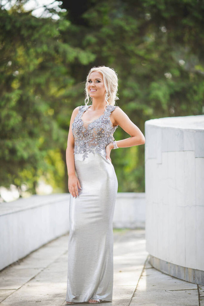 A shallow focus shot of a happy woman on a park pathway in a silver dress - Foto, afbeelding