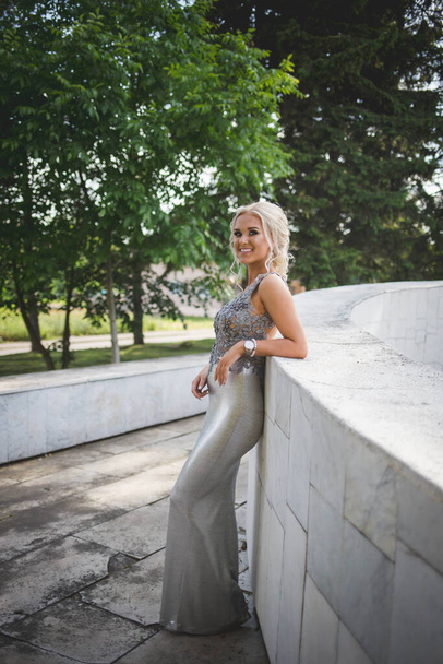 A shallow focus shot of a young woman leaning on a wall in a silver dress - Photo, image