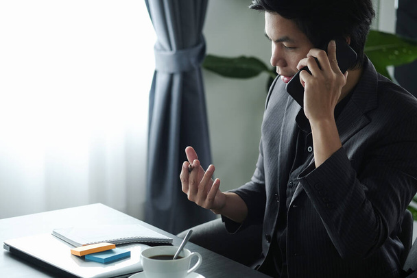 Entrepreneur masculin utilisant un ordinateur portable et parlant sur un téléphone mobile avec son partenaire d'affaires. - Photo, image