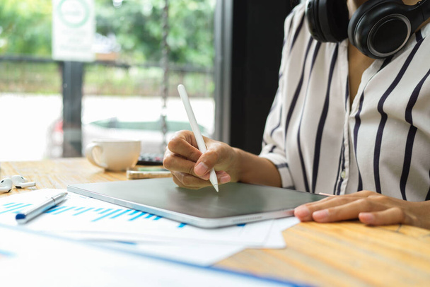 Женщина фрилансер работа с цифровым планшетом, стилус ручка, наушники, финансовый отчет на столе в кафе - Фото, изображение