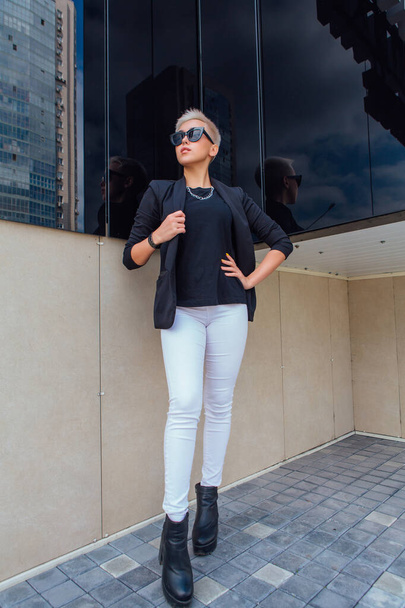 Young stylish business woman with short hair and nose piercing. Confident girl look like lesbian standing near business center with mirror walls - Foto, Imagem