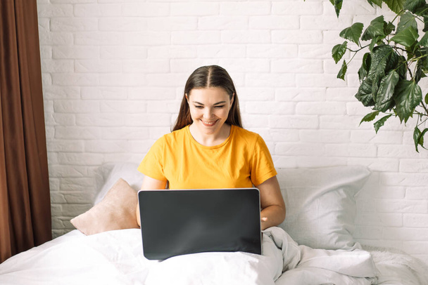 Dziewczyna robi zakupy online za pośrednictwem laptopa podczas siedzenia w łóżku. - Zdjęcie, obraz