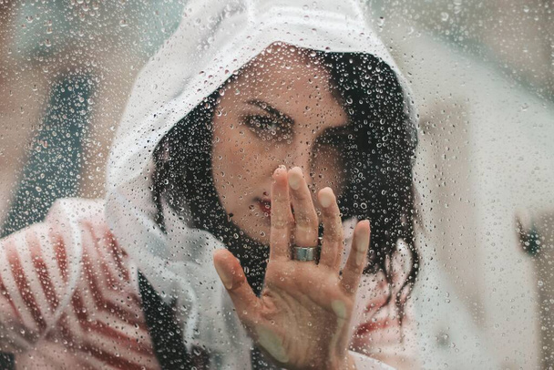 girl in the rain in a raincoat. Drops on glass. - Foto, afbeelding