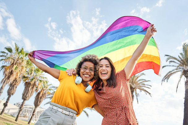 Молодая лесбийская пара празднует день гордости, глядя в камеру с радужным флагом. Концепция гомосексуализма, гей. - Фото, изображение