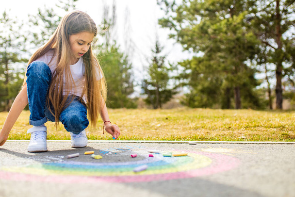 teenage girl drawing a rainbow colored chalk on the asphalt on summer day - Foto, afbeelding