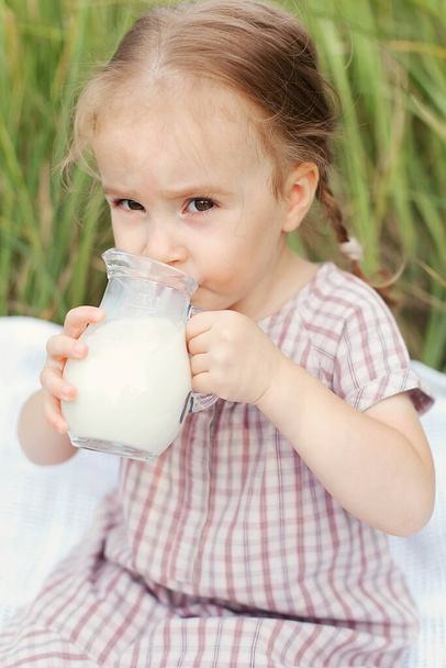 a little girl holds a jug of fresh milk in her hands, a rustic lifestyle, nature, walking on a summer day - Photo, Image