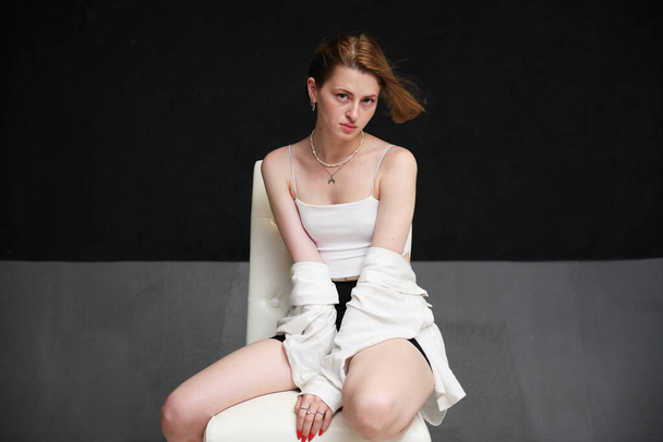 beautiful woman sits on a chair on a dark background in the studio in a light top - Foto, Bild