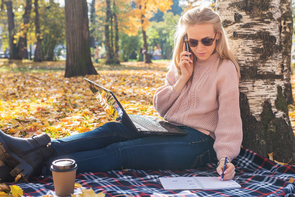 Young woman working with laptop outdoors and holding phone. - Photo, Image