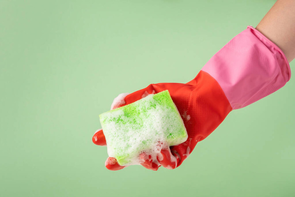 Hand in rubber glove holding green sponge for washing dishes with foam. House cleanining service concept. - Foto, immagini