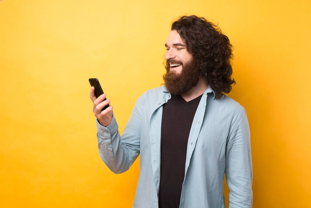 Bearded man use cellphone, answer sms messages have online conversation with friend over yellow background - Fotoğraf, Görsel