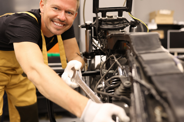 Χαμογελώντας αρσενικό κλειδαρά επισκευή μοτοσικλέτας με κλειδί στο κέντρο εξυπηρέτησης - Φωτογραφία, εικόνα