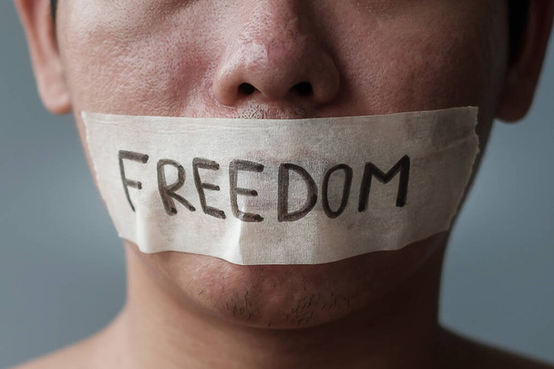 Man with mouth sealed in adhesive tape with Freedom message. Free of speech, freedom of press, Human rights, Protest dictatorship, democracy, liberty, equality and fraternity concepts - Photo, Image