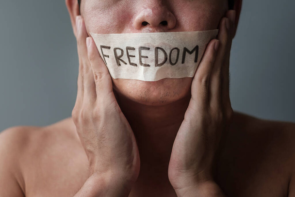 Man with mouth sealed in adhesive tape with Freedom message. Free of speech, freedom of press, Human rights, Protest dictatorship, democracy, liberty, equality and fraternity concepts - Foto, imagen