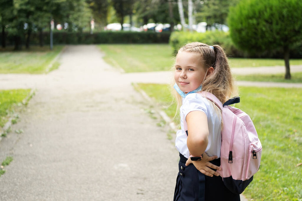 bionda studentessa riccia mette di maschera protettiva in uniforme scolastica con zaino rosa torna a scuola. - Foto, immagini
