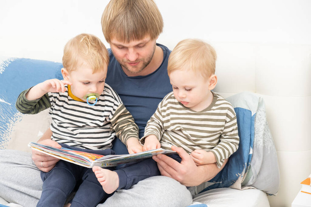 padre leyendo un libro a sus hijos gemelos en la cama en casa, pasar tiempo juntos. - Foto, Imagen