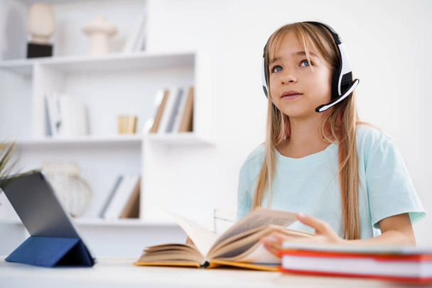 Kis kaukázusi lány fülhallgatóval videóhívás távoli osztály tanár otthon - Fotó, kép