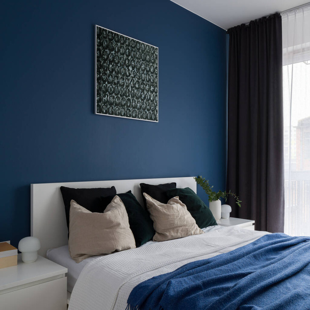 Modern bedroom with white furniture, comfortable bed, window behind curtains and stylish blue wall with art - Foto, Imagem