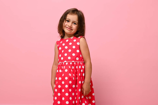 Superbe petite fille européenne, adorable enfant habillé en robe à pois rose, sourires mignons posant sur fond rose avec espace pour le texte. - Photo, image