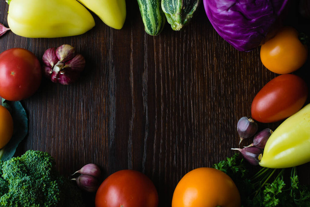 Concept of vegetarianism and proper nutrition. Vegetables tomatoes, garlic, zucchini, cabbage, cilantro, peppers on a dark wooden table top, top view, copy space in the center - 写真・画像