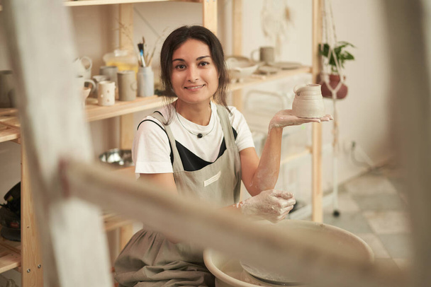 Smiling craftswoman with clay pot in workshop - Zdjęcie, obraz