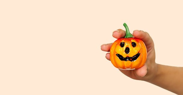 A young girl's hand holds a small orange pumpkin for Halloween against the background of the color trend #FAEBD7 Champagne 2021. A smiling Jack lantern is a symbol of the Halloween holiday. Horror - Fotoğraf, Görsel