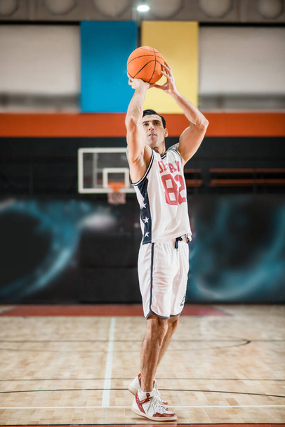 Young athletic man in white sportwear playing basket-ball in the gym - Photo, Image