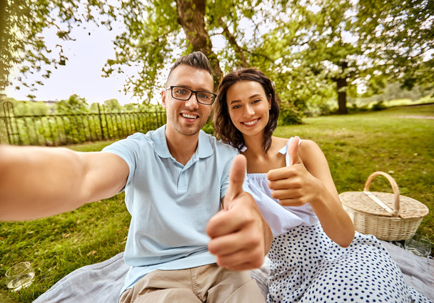 couple taking selfie and showing thumbs up at park - Foto, immagini