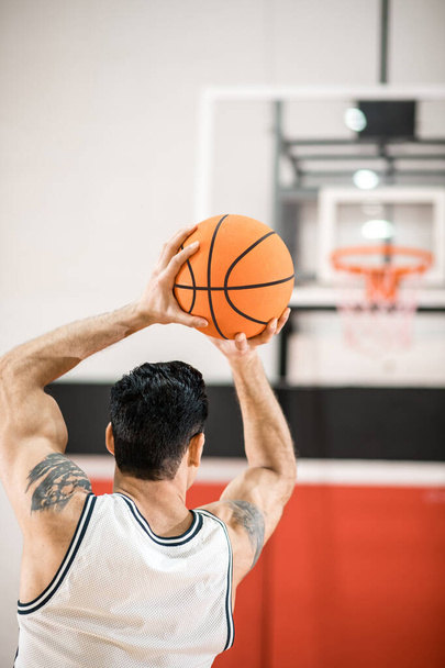 Dark-haired basket-ball player throwitn a ball into the ring - Фото, зображення
