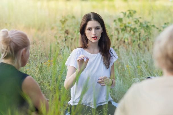Young women are talking in pirirode. The instructor explains before meditation and yoga in an open area. Fitness concept, spiritual practice, psychological help. Copyspace - Fotoğraf, Görsel