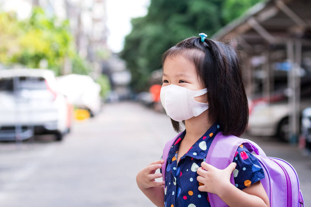 3D衛生的なフェイスマスクを着用し、紫色のスクールバッグを運ぶ少女は、コロナウイルス(COVID-19)として知られている肺炎が発生した後、学校に戻る準備をしています。幸せな学生時代4-5歳 - 写真・画像